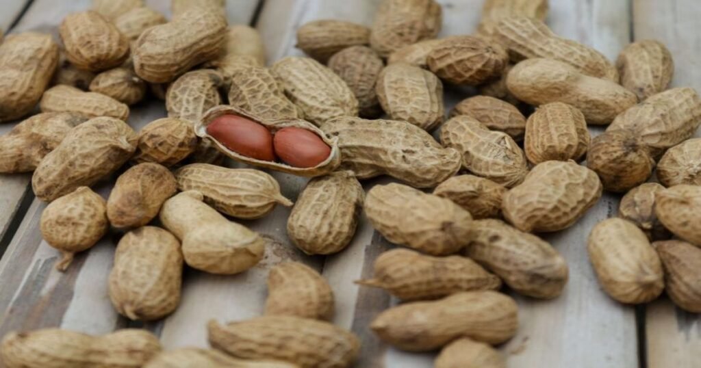 A jar of peanut butter next to whole peanuts on a wooden table.